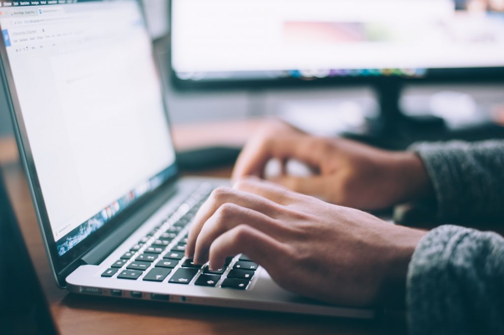 A laptop with a pair of hands typing on it.