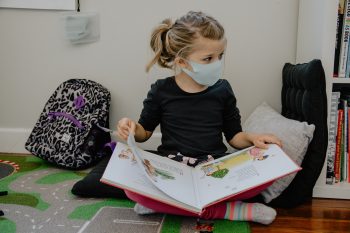 A child sitting wearing a mask with a book on her lap