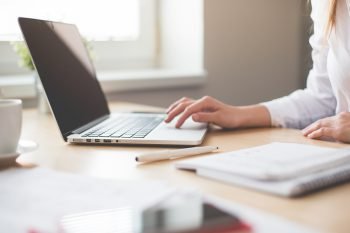 Person on a laptop with a notebook to the side