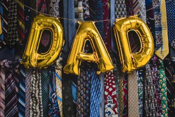 Balloons forming the word "dad" on top of a collection of neck ties