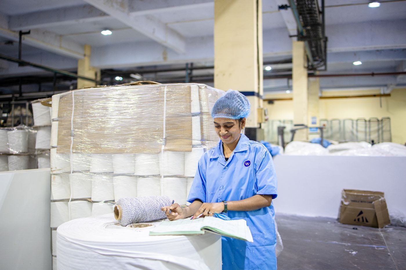 A production lead on the plant floor, logging the day's work in a record book.